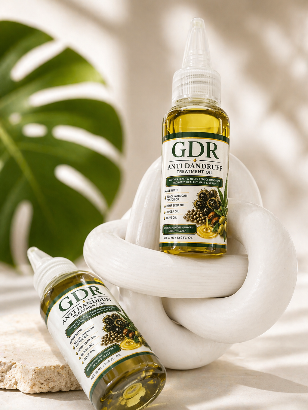 Two bottles of GDR Anti Dandruff Treatment Oil on a white surface with a leaf in the background
