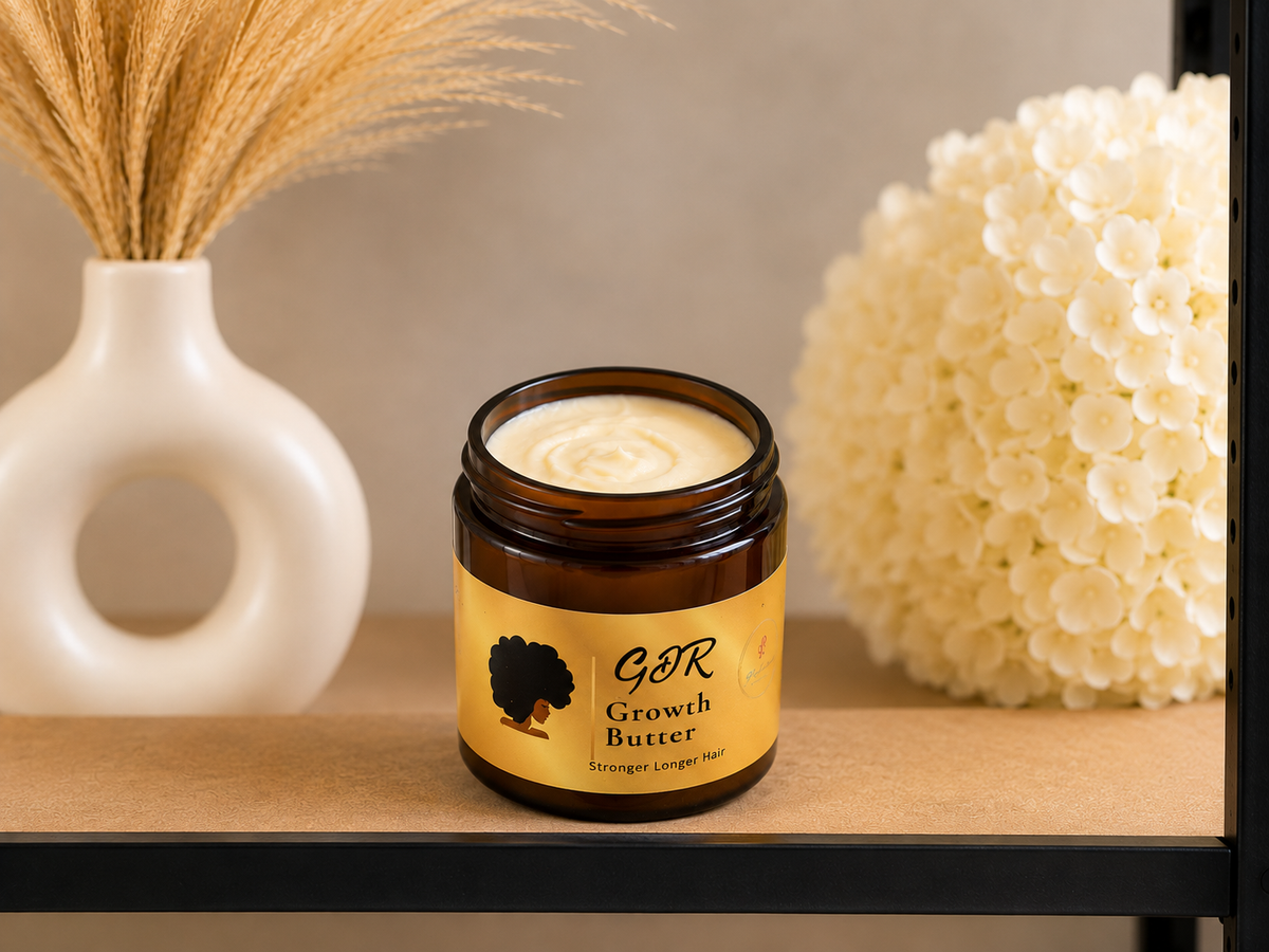 An open amber glass jar of GDR Growth Butter with a yellow label, displayed on a wooden shelf next to a white vase with dried grass and a white flower ball.