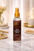 A bottle of GDR Heat Protector Spray stands on a marble surface with a softly blurred warm interior background featuring candles, flowers, and gold-toned decor.