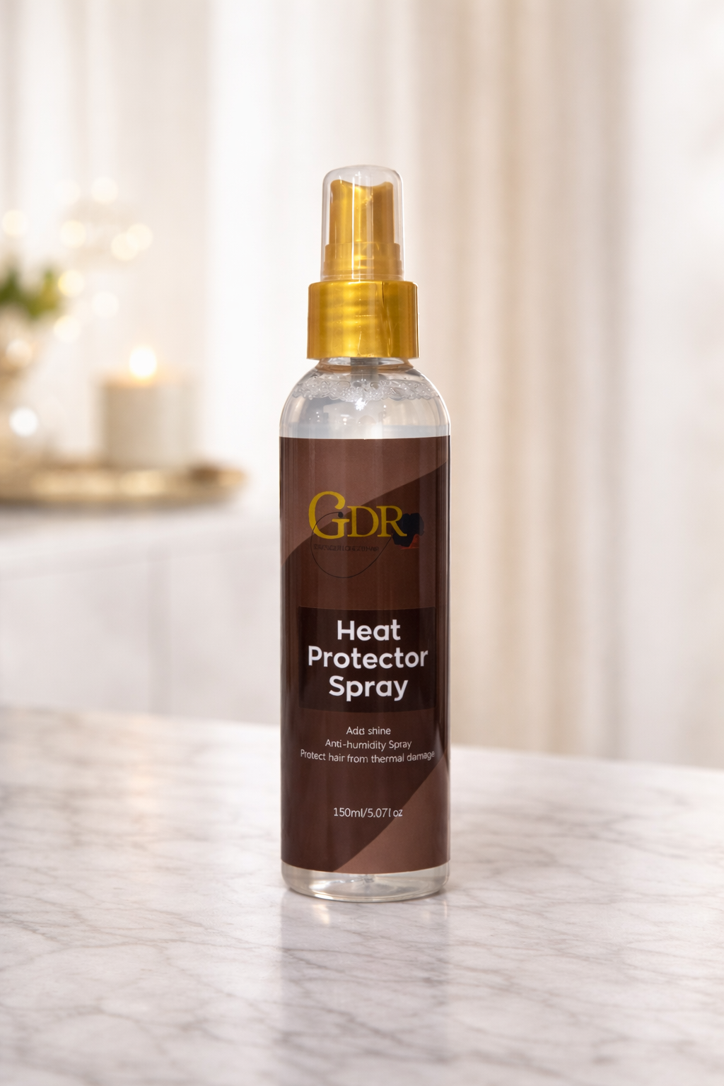 A bottle of GDR Heat Protector Spray with a gold spray nozzle and a dark brown label, standing on a light marble surface with a softly blurred indoor background.